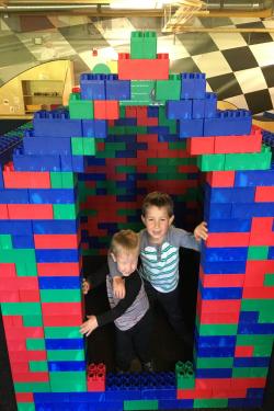 2 children posing in a house made of blocks